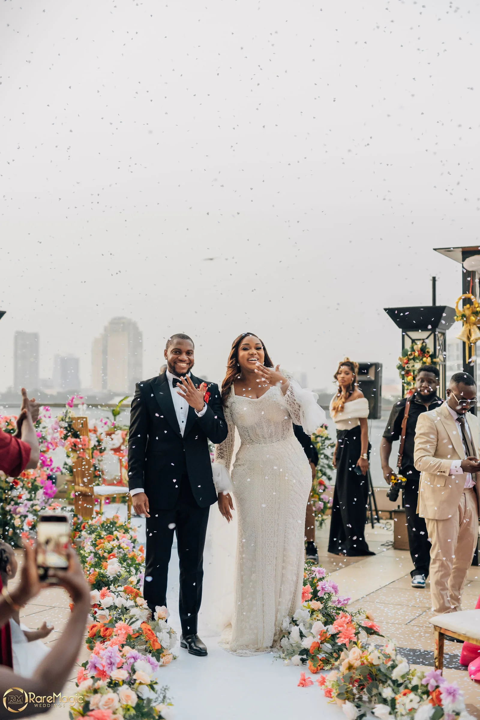 Bride and groom laughing under a shower of confetti beneath a chandelier