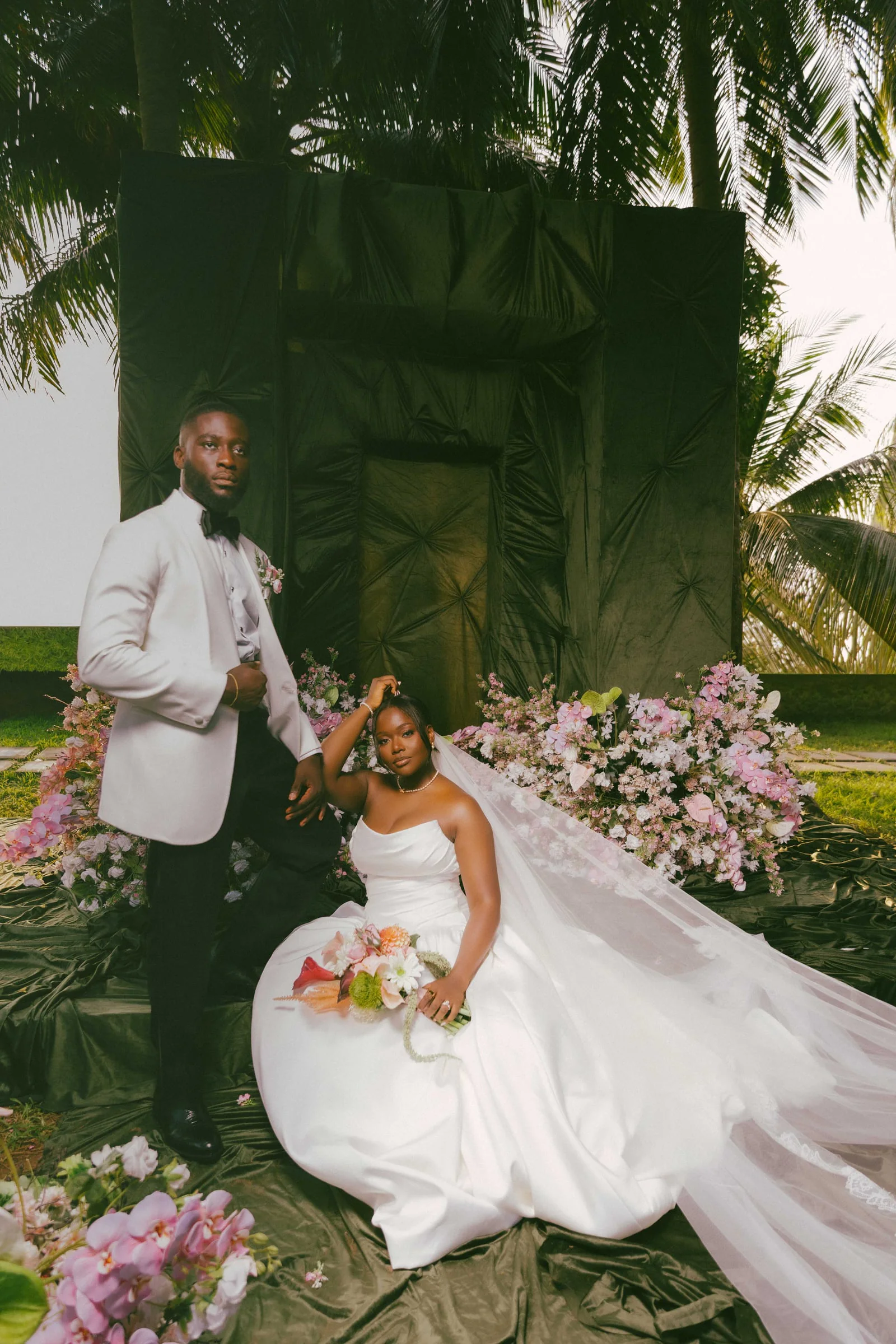 Couple posing before a green backdrop under palm trees