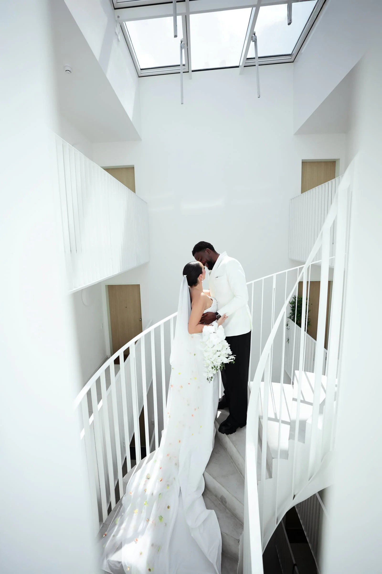 Bride and groom embracing on a spiral staircase beneath a skylight